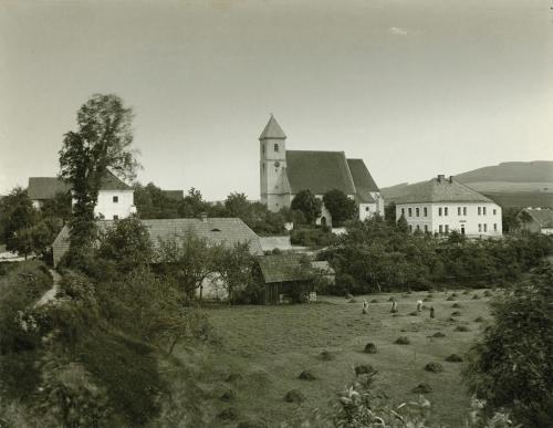 Mlýn pod hrází rybníka na předválečné fotografii spolu s dalšími třemi významnými budovami obce – vlevo fara, uprostřed kostel a napravo škola. | Mühle unter dem Damm des Teiches auf einem Vorkriegsfoto mit drei anderen wichtigen Gebäuden des Dorfes – links das Pfarrhaus, in der Mitte die Kirche und rechts die Schule.